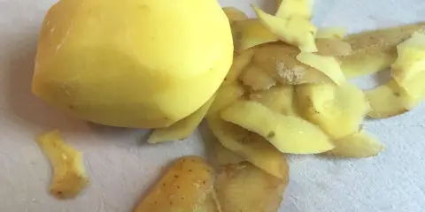 Ein geschältes Kartoffelstück liegt neben einem Haufen Kartoffelschalen, die wie ein kleines, flauschiges Kaninchen aussehen.