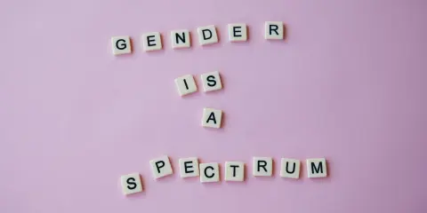 Litery na różowym tle układają się w napis "GENDER IS A SPECTRUM". To przypomnienie, że tożsamość płciowa nie jest binarna, a doświadczenie dysforii płciowej jest częścią tej złożoności.