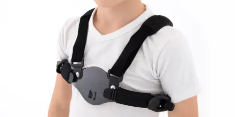 Dziecko w białej koszulce nosi czarny stabilizator klatki piersiowej, który pomaga korygować wypukłą klatkę piersiową.