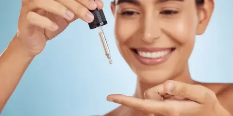 Uśmiechnięta kobieta aplikuje serum z pipetki na palec. To jej sekret na gładką skórę z retinalem 0,2.