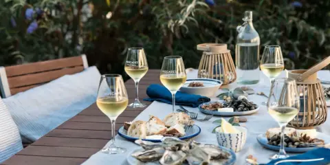 Ein gedeckter Tisch im Freien mit Austern, Brot und Gläsern voller Muscadet, einem Wein aus der Melon de Bourgogne Traube.