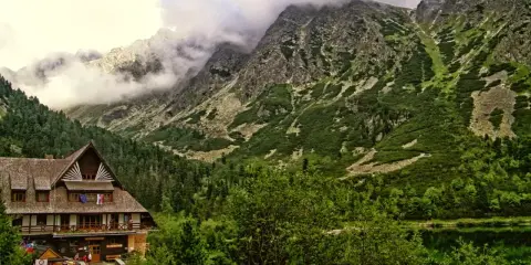 Drewniany budynek schroniska tatry w otoczeniu zielonych zboczy i skalistych gór, nad spokojnym jeziorem.