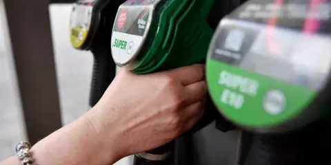 Hand greift nach Zapfhahn. Der steigende CO2-Preis macht sich beim Tanken bemerkbar.