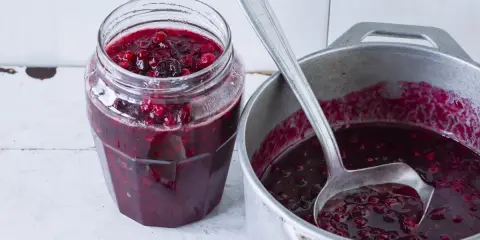 Słoik z konfiturą żurawinową i chochla w garnku z konfiturą.