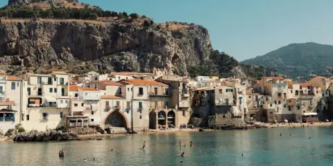 Un incantevole borgo da visitare in Sicilia, con case color pastello affacciate sul mare cristallino e una maestosa roccia a fare da sfondo.