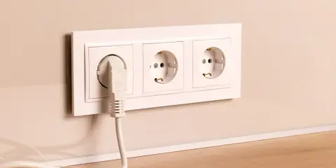 Prise électrique blanche avec un câble branché, installée à la hauteur du plan de travail.