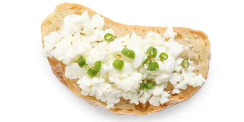 Kanapka z białym serkiem i szczypiorkiem na białym tle.