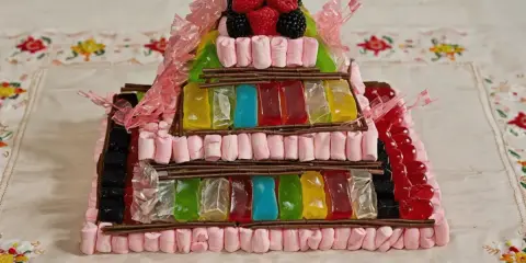 Tarta de chuches escalonada, con capas de gominolas de colores, marshmallows rosas y frutos rojos en la cima.