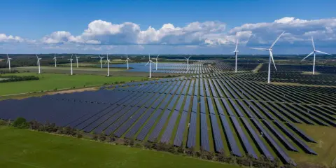 Großes Feld mit Windkraftanlagen und Photovoltaik-Modulen unter blauem Himmel mit Wolken.
