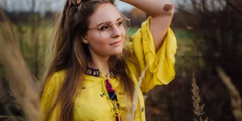 Portret dziewczyny w okularach i żółtej sukience, wśród traw. Różne rodzaje portretów w fotografii mogą uchwycić taką naturalną, swobodną chwilę.