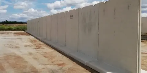 Larga pared de separador de hormigón prefabricado, instalada sobre una base de hormigón, con un cielo azul y nubes blancas al fondo.