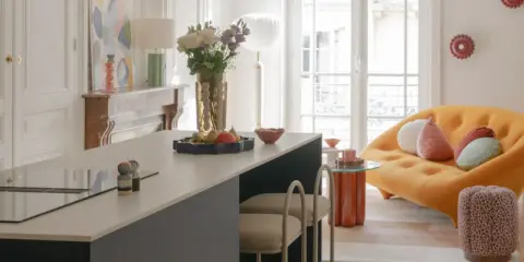 Aménagement salon salle à manger cuisine : îlot central moderne, canapé orange design, cheminée ancienne et art abstrait.