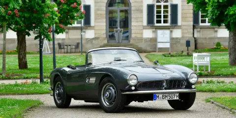 Un elegante BMW descapotable gris, un clásico de Alemania, aparcado frente a un edificio histórico con árboles en flor.