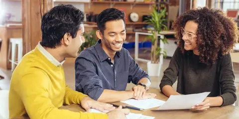 Trois personnes discutent autour d'une table, examinant des documents. Ils semblent planifier leur projet et se demandent combien emprunter avec 2500 euros par mois.