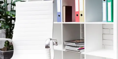 Scrivania ordinata con sedia bianca e scaffali pieni di raccoglitori colorati, perfetti per chi cerca idee su come organizzare i documenti di casa.