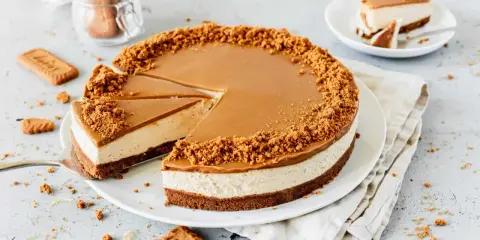 Ein köstlicher Lotus Cheesecake mit Karamellglasur und Keksbröseln. Ein Stück wurde bereits entnommen, daneben liegen weitere Kekse.