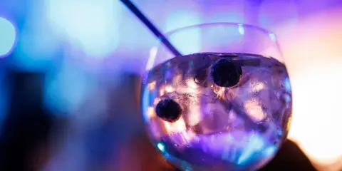 Ein Glas mit Eis und Beeren, in dem das tonic water leuchtet, vor einem verschwommenen, bunten Hintergrund.