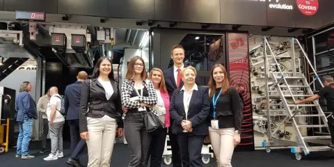 Grupa osób na targach poligraficznych, pozuje przed maszyną drukarską Comexi F1.
