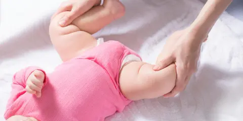 Delikatne badanie nóżek niemowlaka, uwaga skupiona na asymetrii fałdów udowych.