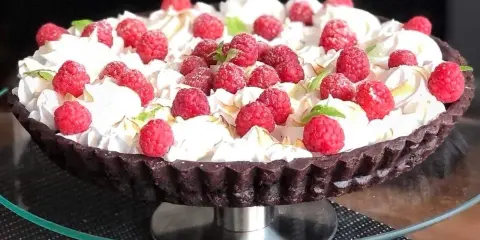 Pyszna tarta czekoladowa z malinami, udekorowana bitą śmietaną i listkami mięty. Idealna na deser.