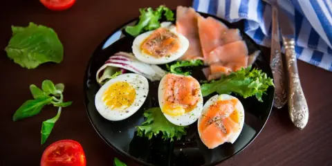 Jajka na twardo z łososiem i sałatą, idealne na dietę low carb. Pomidorki i zielenina dopełniają danie.