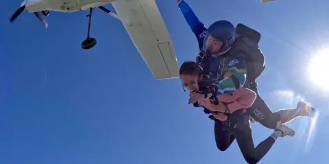 Ein Tandem-Fallschirmsprung – die perfekte Antwort auf die Frage, was schenkt man zum bestandenen Abitur. Zwei Menschen genießen den freien Fall vor strahlend blauem Himmel.