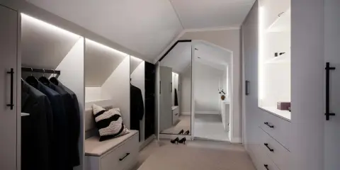 En stilren walk-in-closet med inbyggd sittbänk och garderobslösningar som utnyttjar kattvindens vinklar.