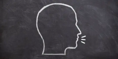 Kredą narysowany profil głowy z liniami symbolizującymi dźwięk wydobywający się z ust, ukazujący fałdy głosowe podczas mówienia.