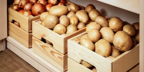 Drewniane skrzynki z cebulą i ziemniakami, idealne do przechowywania warzyw w kuchni.