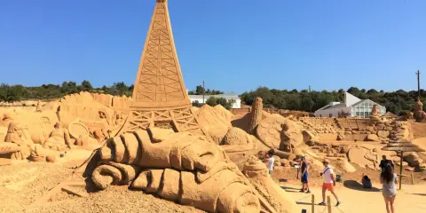 Beeindruckende Sandskulpturen, darunter der Eiffelturm, im Sand City Algarve. Besucher bestaunen die Kunstwerke.