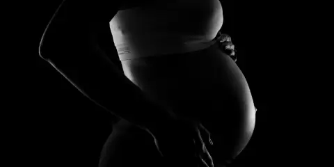 Silhuett av en gravid kvinna som håller sin mage. En bakåtlutad livmoder är tydligt synlig under den sträckta huden.