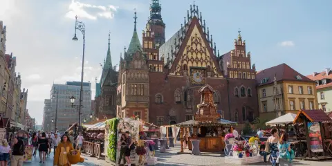 Wrocław stare miasto tętni życiem. Ludzie spacerują po Rynku, podziwiając zabytkowy ratusz i kolorowe kramy.