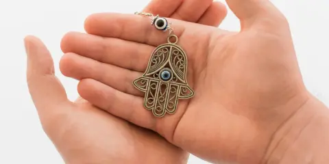 Dłonie trzymające ozdobny amulet w kształcie ręki Fatimy z niebieskim okiem.
