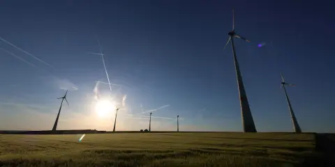 Windräder im Feld bei Sonnenuntergang, ein Symbol für den Windkraftausbau Deutschland. Kondensstreifen kreuzen den blauen Himmel.