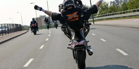 Motocyklista wykonuje jazdę na jednym kole z nogami w powietrzu. Ryzykowne wyczyny mogą skończyć się mandatem.