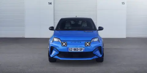La nuova Alpine A290, un'auto elettrica sportiva blu brillante, attende il suo momento davanti a un garage con porte chiuse.