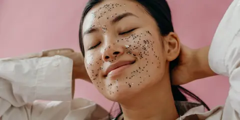 Une jeune femme au visage couvert d'un masque exfoliant scintillant, profitant d'un moment de détente. Elle nous rappelle pourquoi exfolier sa peau est essentiel pour un teint éclatant.