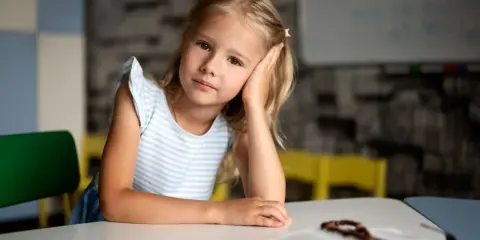 Dziewczynka z autyzmem opiera głowę na dłoni, patrząc w dal. Obok leży otwarta książka z różańcem.