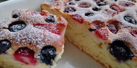 Puszyste ciasto na maślance z jagodami i malinami, posypane cukrem pudrem. Idealne na deser.