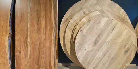 Plusieurs plateaux de table ronde en bois, empilés, illustrent la définition d'une table ronde. Des planches de bois brut sont aussi visibles.