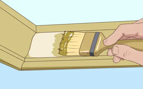 Main tenant pose du mastic sur une moulure en bois avec un pinceau.
