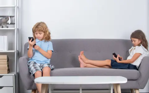 Dzieci na kanapie, każde pochłonięte telefonem. Czy to znak, że od ilu lat dziecko może zostać samo w domu?