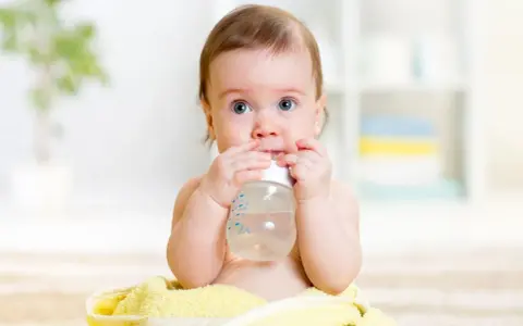 Ein süßes Baby mit blauen Augen hält eine Flasche und trinkt. Es scheint, als ob dieses Baby zu viel trinkt, aber es genießt jeden Schluck.