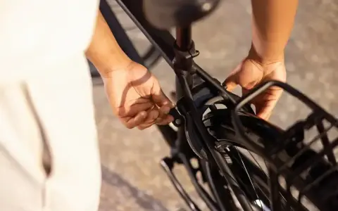 Ręce zaciskają blokadę roweru na ramie, zabezpieczając go przed kradzieżą.
