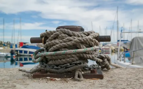 Grosse amarre enroulée sur une bitte d'amarrage, prête à supporter le poids d'un bateau. Le diamètre de la corde suggère une grande résistance.