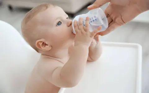 Niemowlę pije wodę z butelki. Od kiedy dziecko może pić wodę mineralną nieprzegotowaną? Od 6. miesiąca życia, gdy zaczyna rozszerzać dietę.