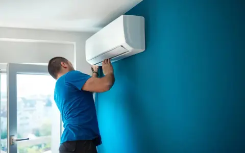 Técnico con carnet instalador aire acondicionado ajusta unidad interior en pared azul.