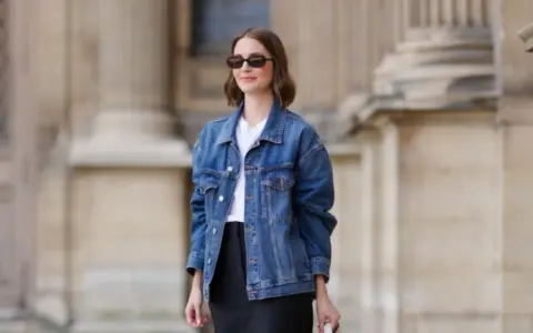 Donna con occhiali da sole indossa un outfit giacca jeans donna, t-shirt bianca e gonna nera.