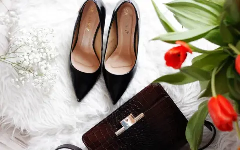 Eleganckie czarne szpilki, brązowa kopertówka i bukiet czerwonych tulipanów – idealne buty na prezent.