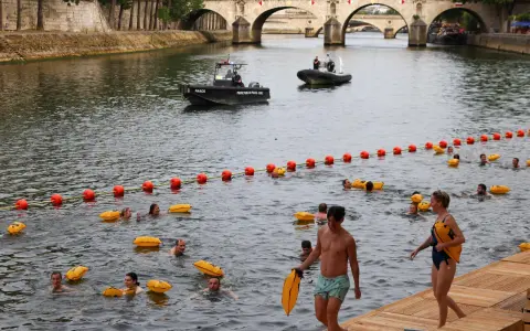 Gente nadando en el Sena de París, con boyas naranjas y una lancha de policía.